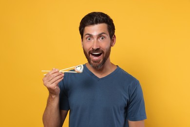 Photo of Emotional man holding sushi roll with chopsticks on orange background