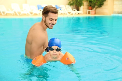 Photo of Happy father teaching his son to swim with inflatable sleeves in pool