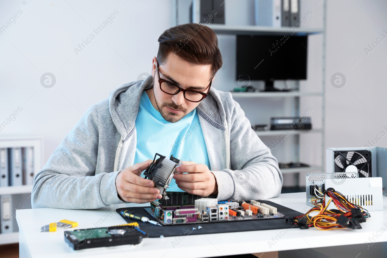 Photo of Male technician repairing motherboard at table indoors