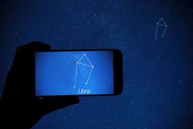 Woman using stargazing app on her phone at night, closeup. Identified stick figure pattern of Libra constellation on device screen