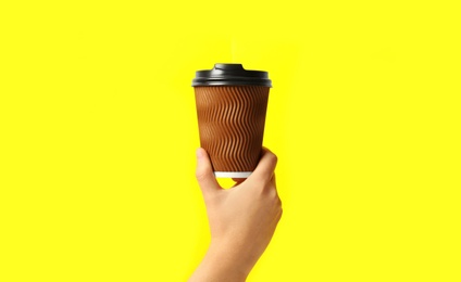 Woman holding takeaway paper coffee cup on yellow background, closeup