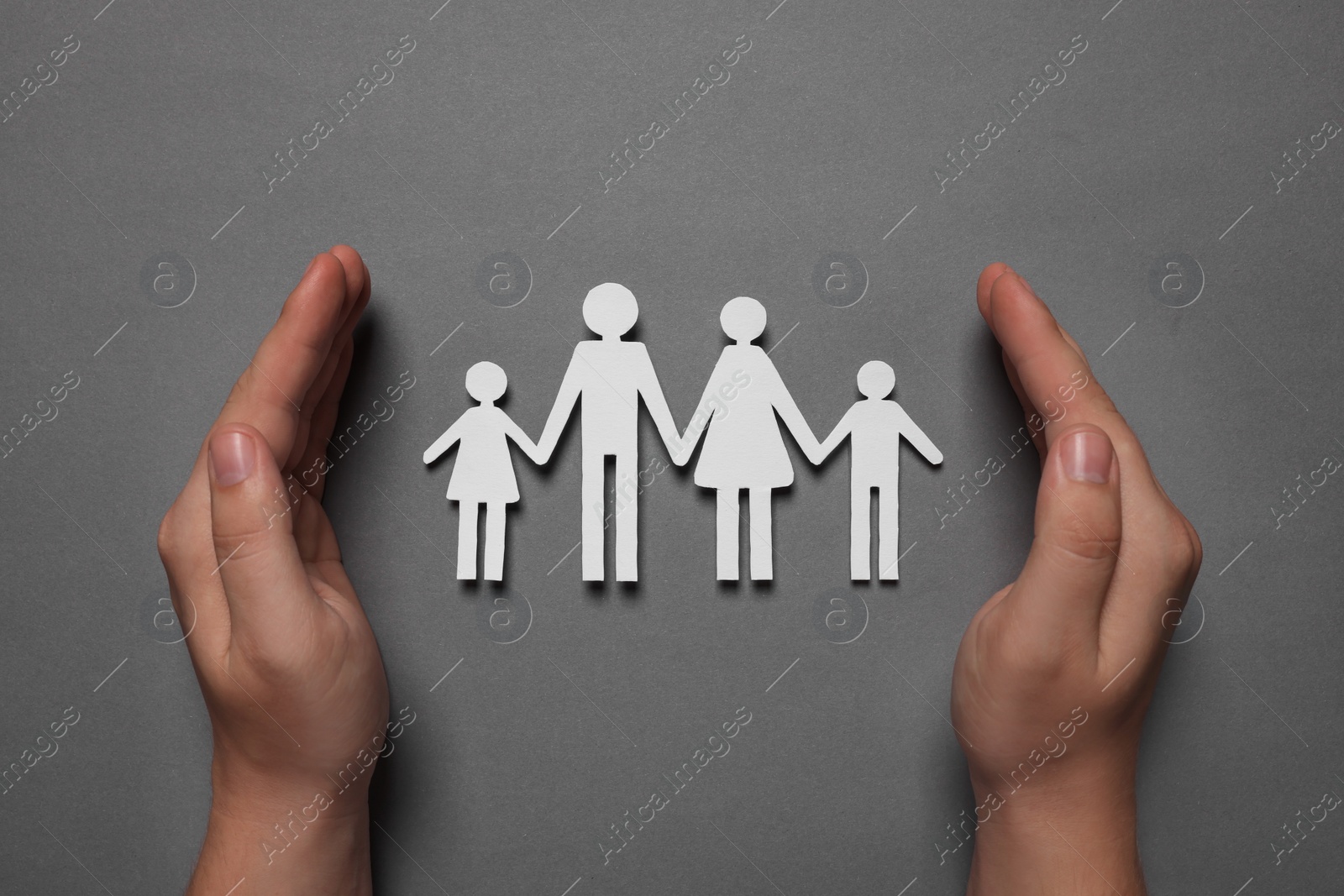 Photo of Man protecting paper family figures on grey background, top view. Insurance concept