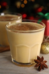 Tasty eggnog with cinnamon and anise on white wooden table against blurred festive lights, closeup