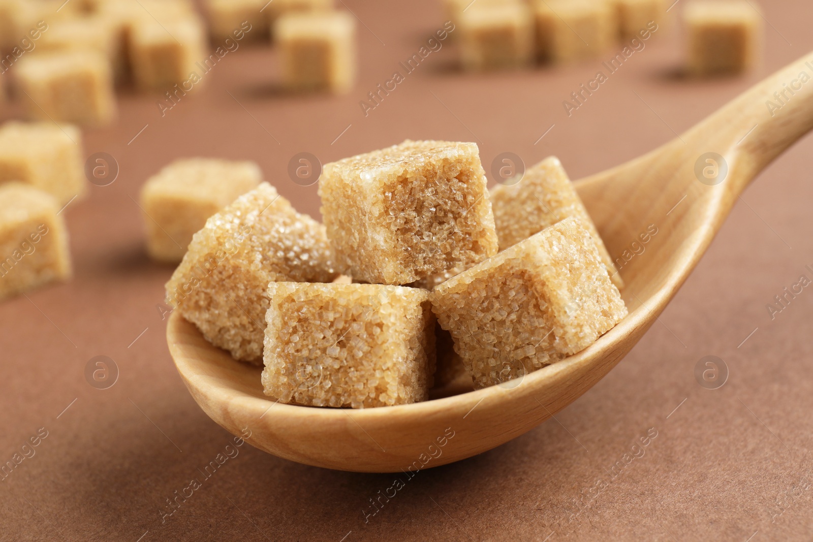 Photo of Brown sugar cubes in spoon on color background, closeup