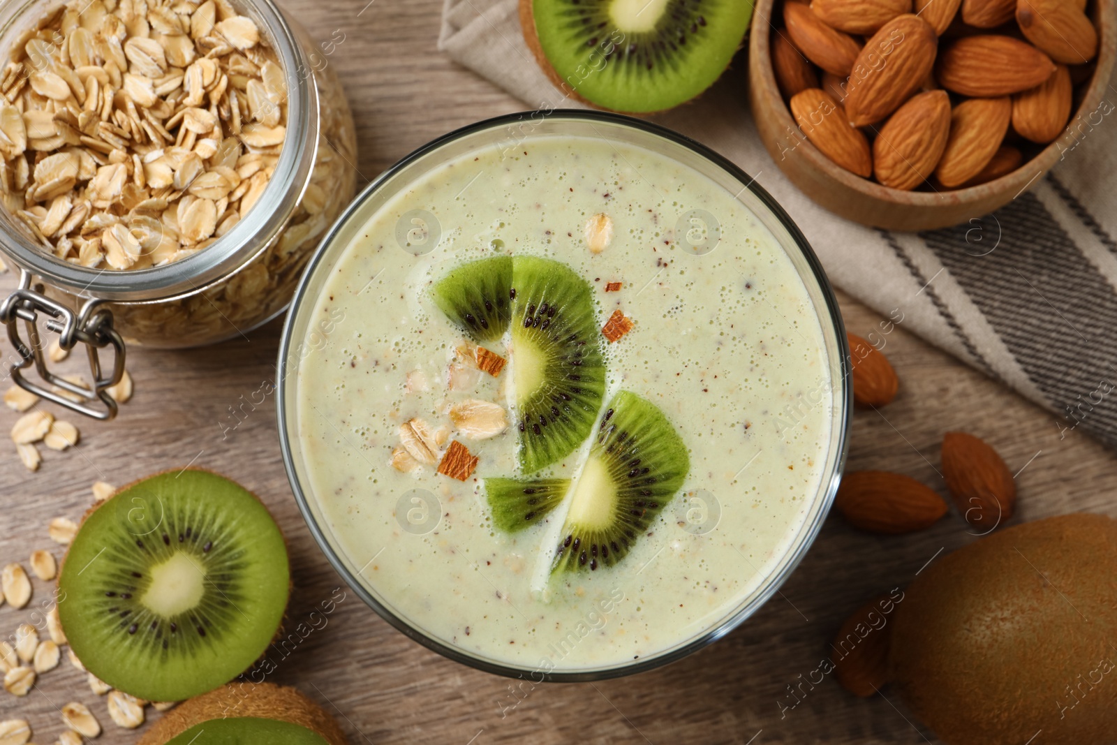 Photo of Glass of tasty kiwi smoothie with oatmeal on wooden table, flat lay