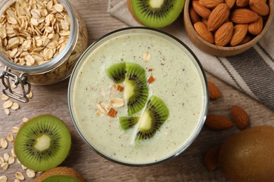 Photo of Glass of tasty kiwi smoothie with oatmeal on wooden table, flat lay