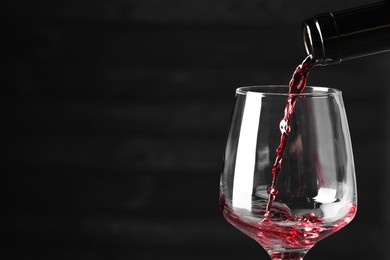 Photo of Pouring red wine into glass against dark background, closeup. Space for text