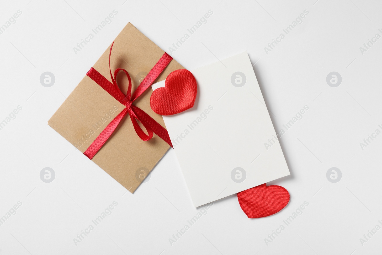 Photo of Blank card, envelope and red decorative hearts on white background, flat lay with space for text. Valentine's Day celebration