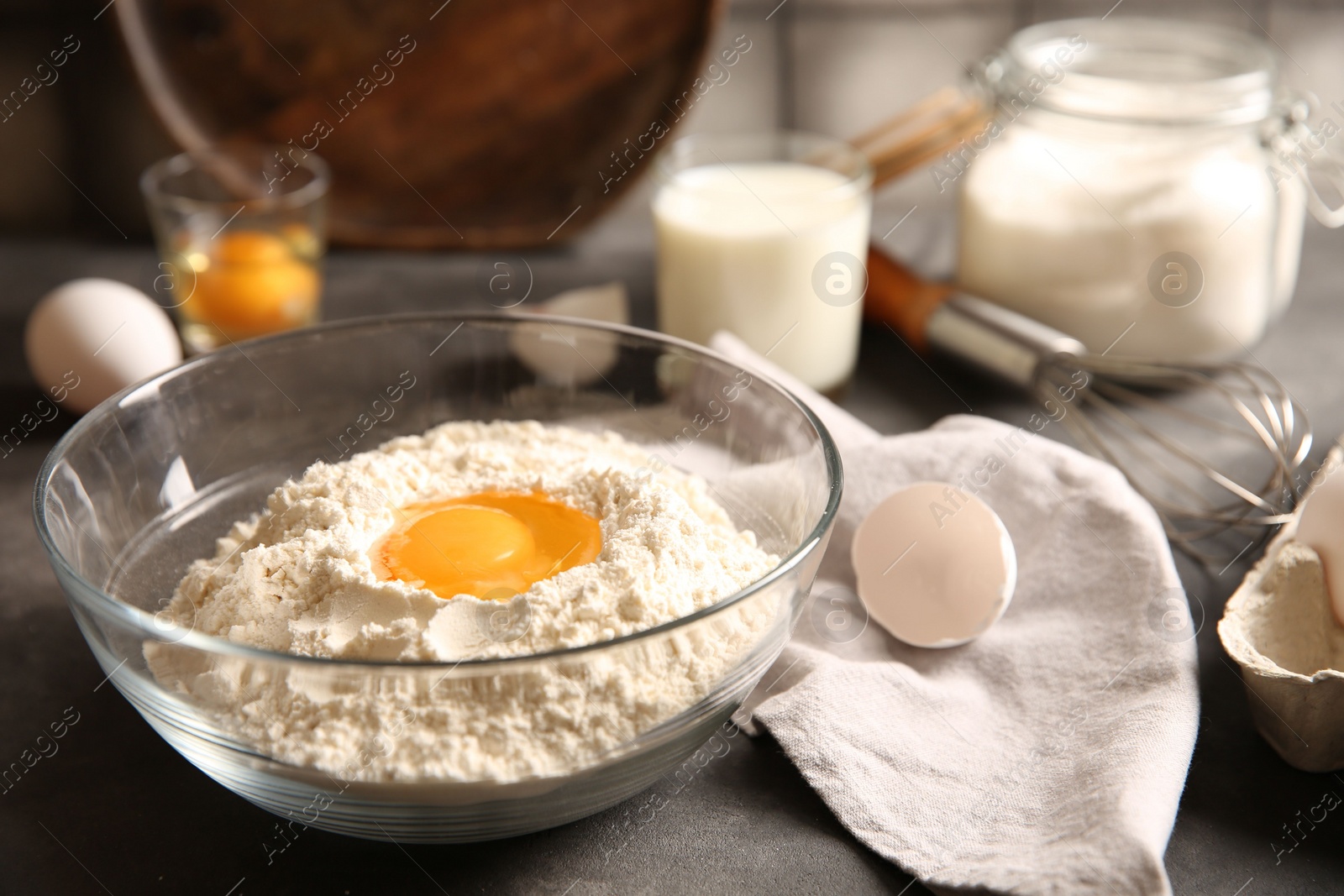 Photo of Making dough. Flour with egg yolk in bowl on grey table, closeup