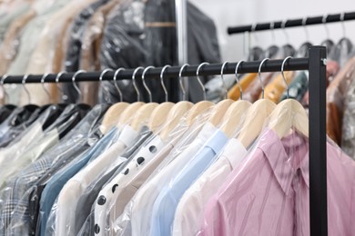 Photo of Dry-cleaning service. Many different clothes in plastic bags hanging on rack indoors, closeup