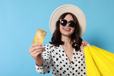 Beautiful young woman with paper shopping bags and credit card on light blue background