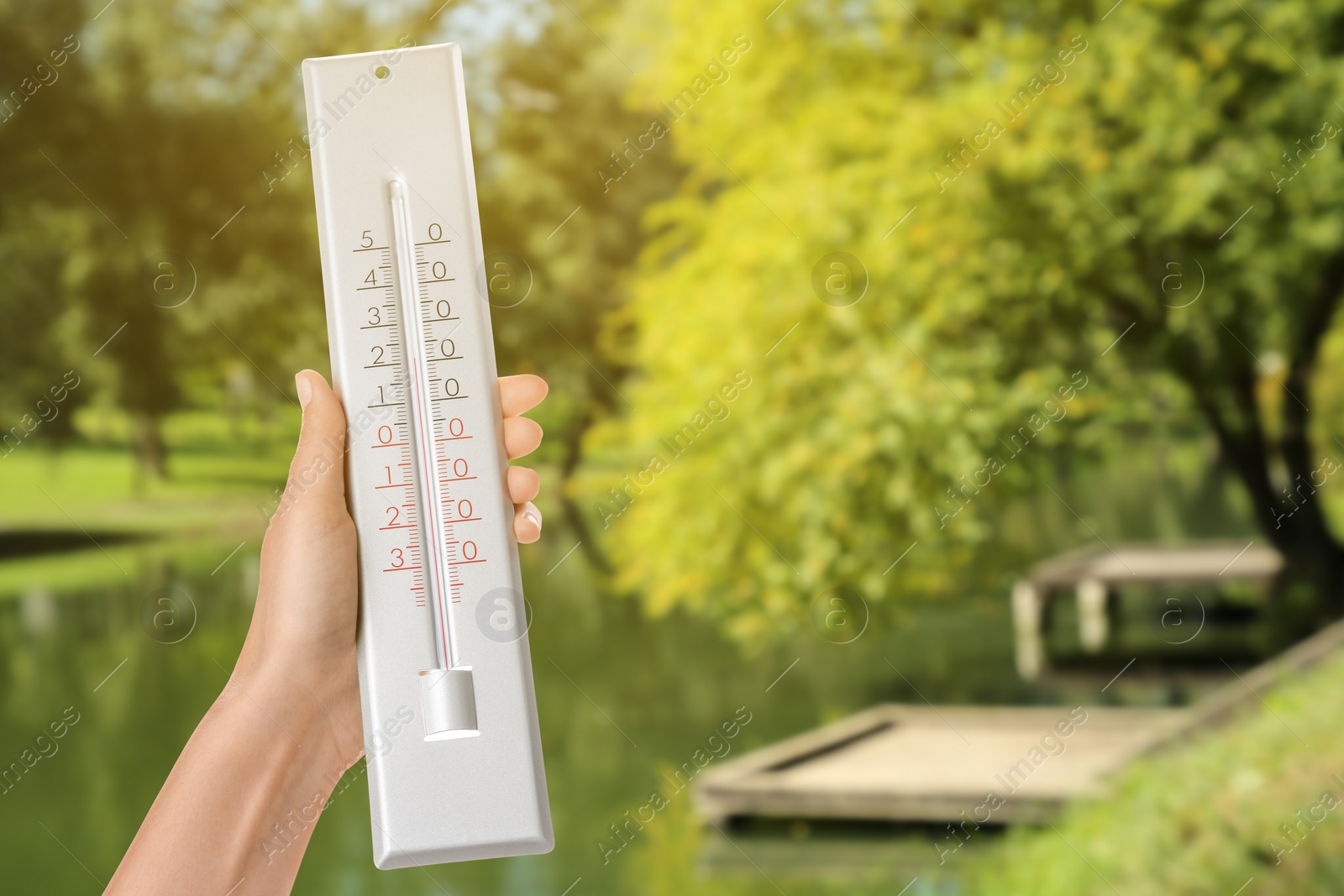 Image of Woman holding thermometer in park on sunny day, closeup