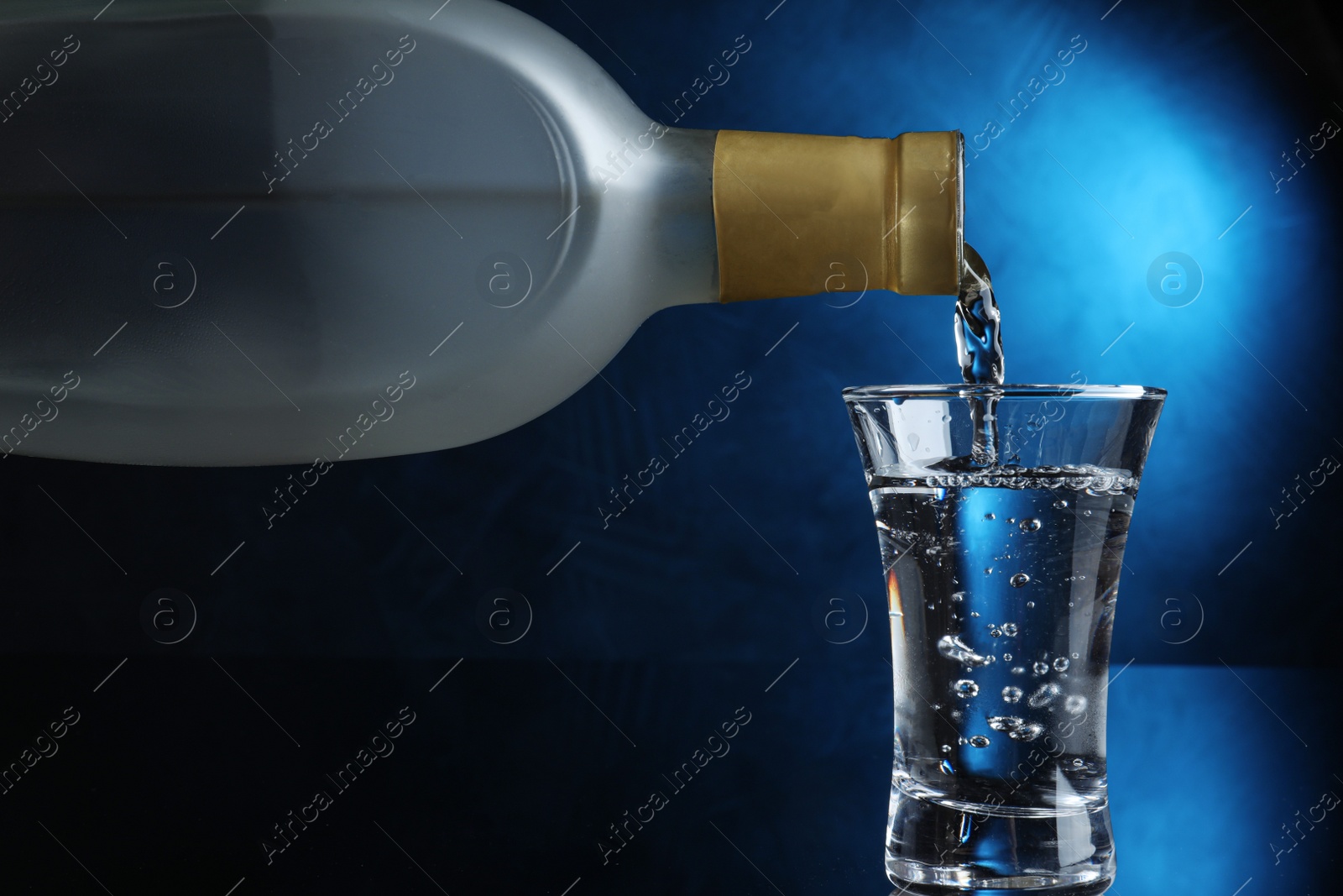 Photo of Pouring vodka into shot glass on dark background with blue light