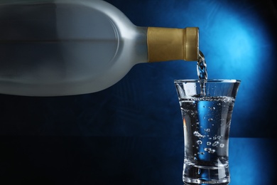 Photo of Pouring vodka into shot glass on dark background with blue light