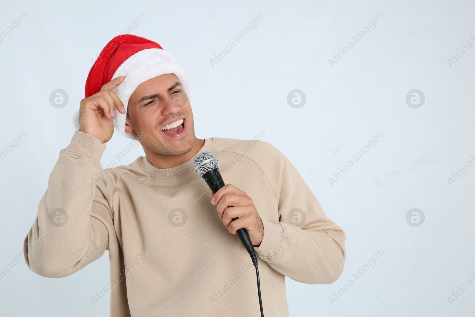 Photo of Emotional man in Santa Claus hat singing with microphone on white background, space for text. Christmas music