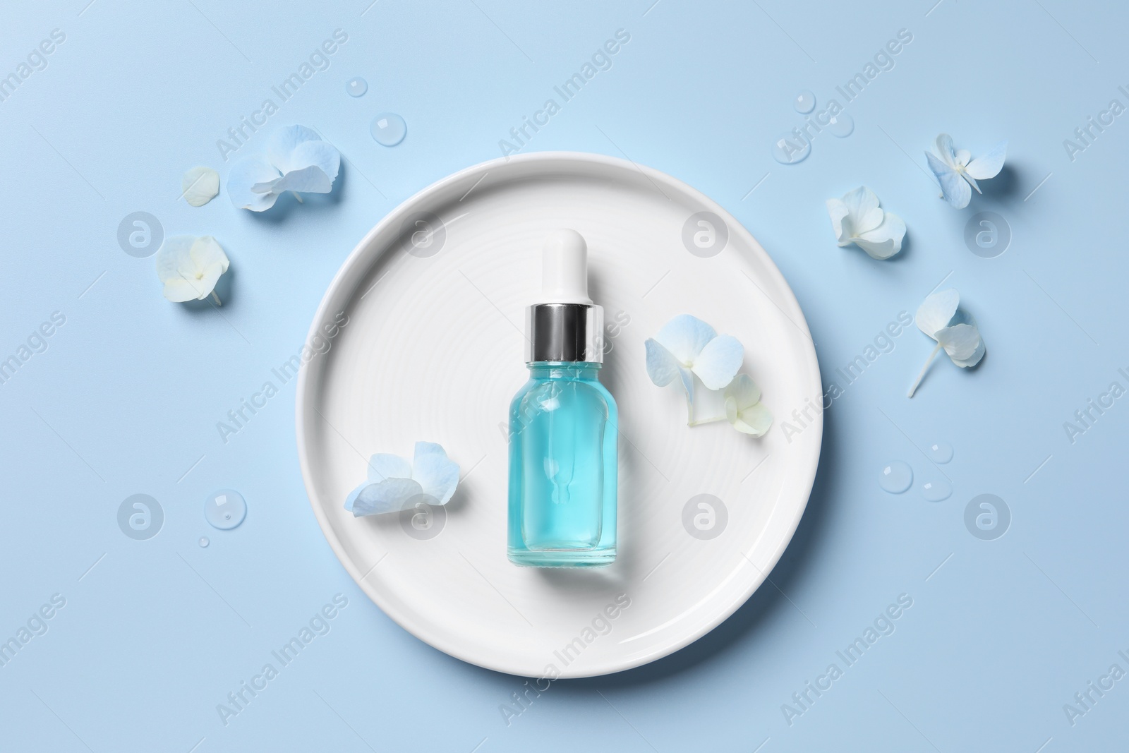 Photo of Bottle of cosmetic serum and beautiful flowers on light blue background, flat lay