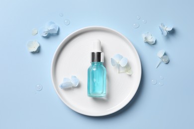 Photo of Bottle of cosmetic serum and beautiful flowers on light blue background, flat lay