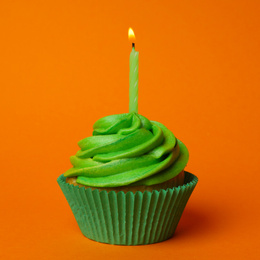 Delicious birthday cupcake with green cream and burning candle on orange background