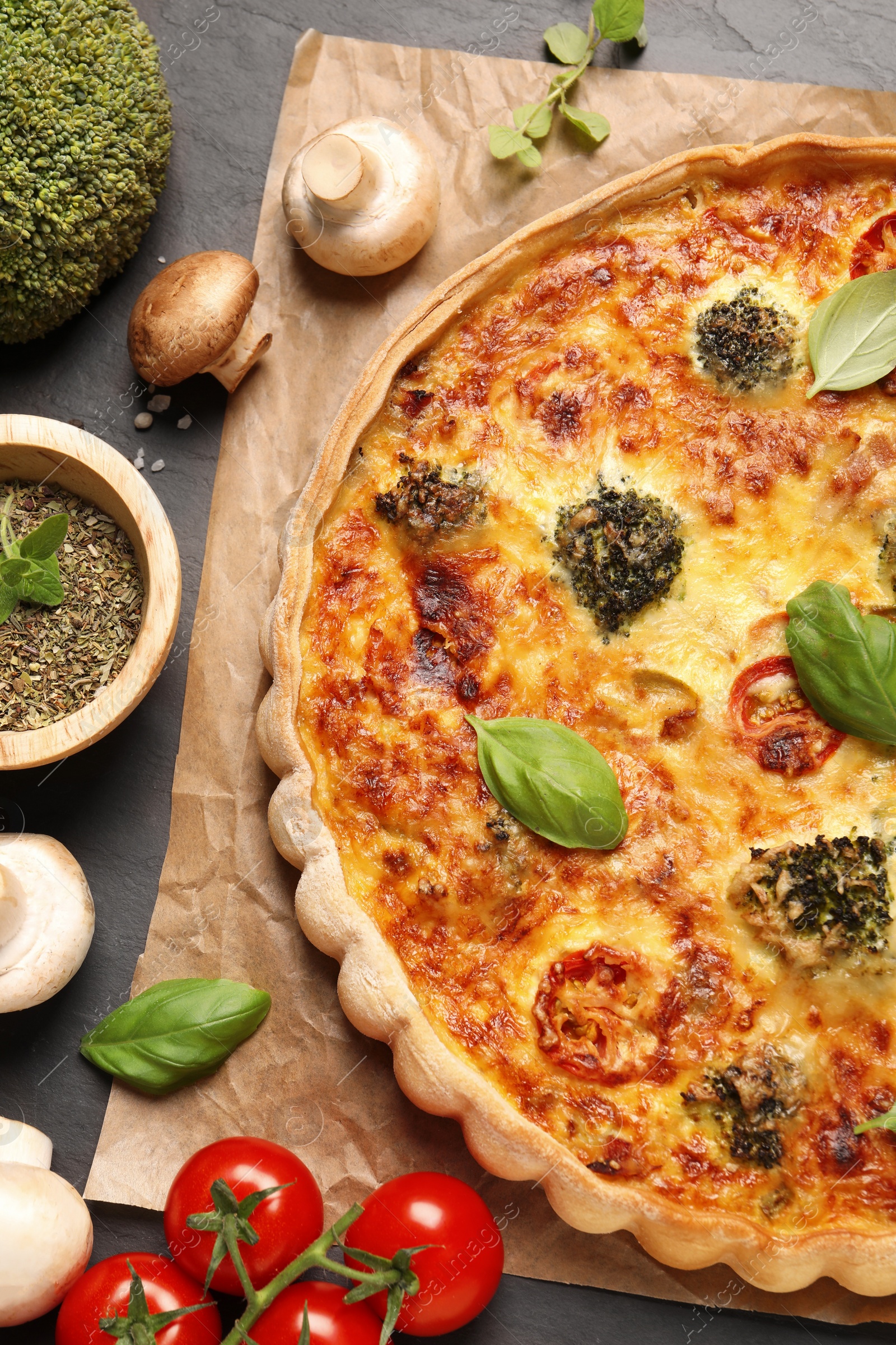 Photo of Delicious homemade vegetable quiche, different vegetables and seasoning on black table, flat lay