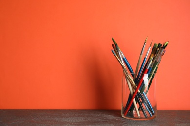 Glass with paint brushes on table against color background. Space for text