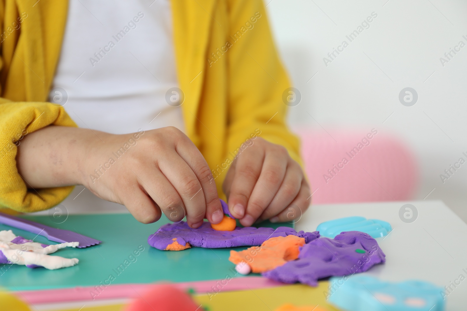 Photo of Little girl sculpting with play dough at table indoors, closeup