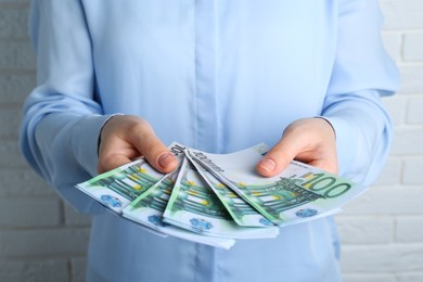Woman holding 100 Euro banknotes near white brick wall, closeup. Money exchange