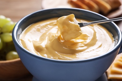 Photo of Dipping bread into pot with cheese fondue on table, closeup