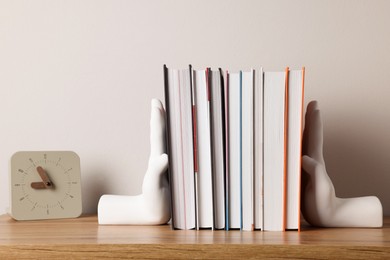 Photo of Beautiful hand shaped bookends with books and clock on table near light wall