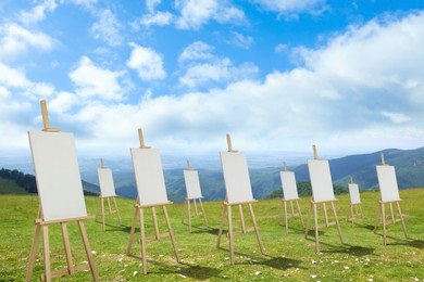 Image of Wooden easels with blank canvases in mountains on sunny day 