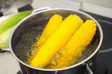 Pot with boiling corn cobs in kitchen, closeup