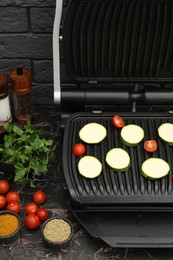 Photo of Electric grill with vegetables and spices on black marble table