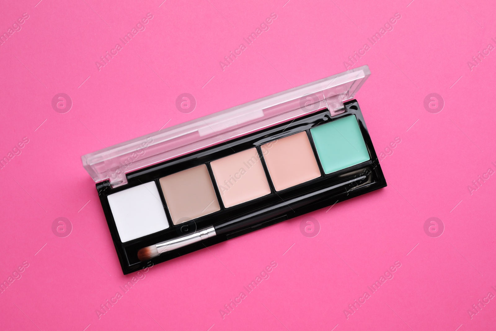 Photo of Colorful contouring palette with brush on pink background, top view. Professional cosmetic product