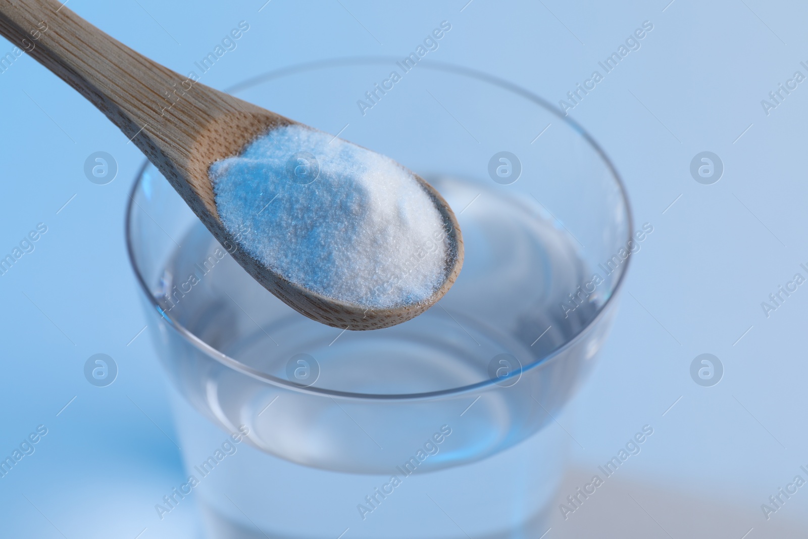 Photo of Spoon with baking soda over glass of water on light blue background, closeup