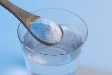 Spoon with baking soda over glass of water on light blue background, closeup