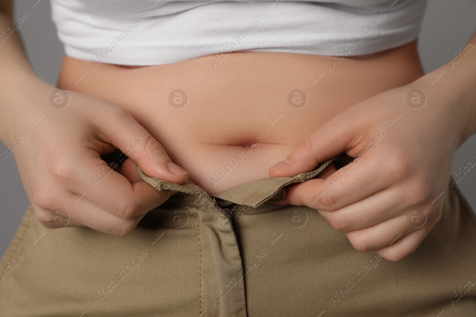 Photo of Overweight woman trying to button up tight pants on grey background, closeup