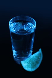 Photo of Shot glass of vodka with lime slice on dark background