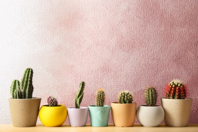 Different potted cacti on table near color background, space for text. Interior decor