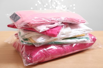 Photo of Stack of folded clothes in plastic bags on wooden table against beige background with blurred lights