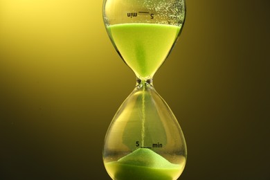 Photo of Hourglass with light green flowing sand on color background, closeup