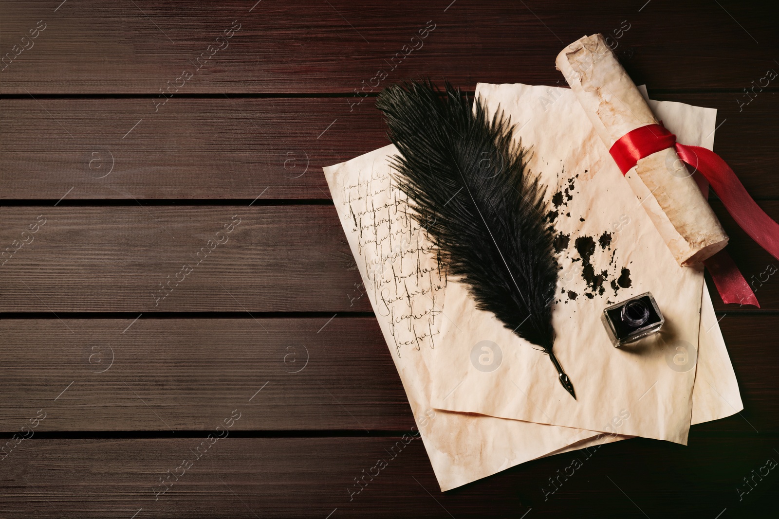 Photo of Inkwell, feather pen and vintage parchment with ink stains on wooden table, top view. Space for text