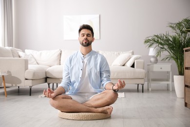Photo of Young man meditating on straw cushion at home