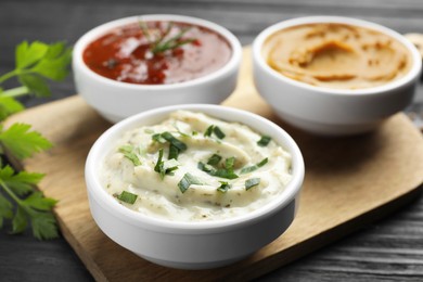 Photo of Different tasty sauces in bowls and parsley on black wooden table, closeup