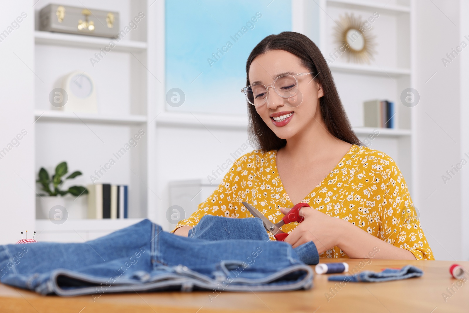 Photo of Happy woman cutting hem of jeans at table indoors