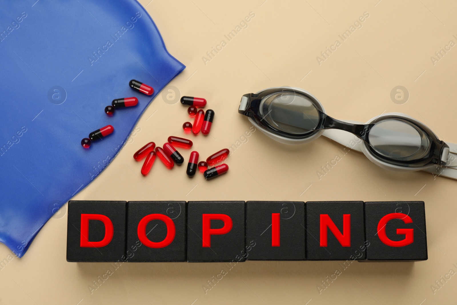 Photo of Black wooden cubes with word Doping, drugs, swimming goggles and cap on beige background, flat lay