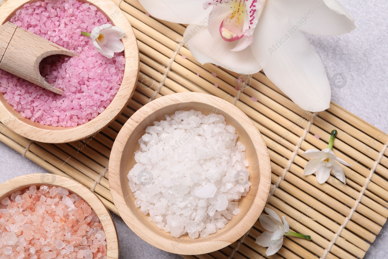 Photo of Different types of sea salt and flowers on light table, flat lay. Spa products