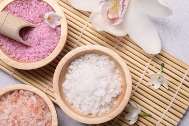 Photo of Different types of sea salt and flowers on light table, flat lay. Spa products