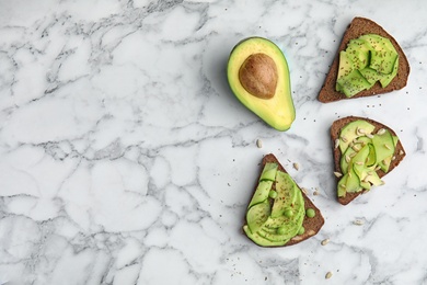 Tasty crisp rye toasts with avocado on marble table, top view