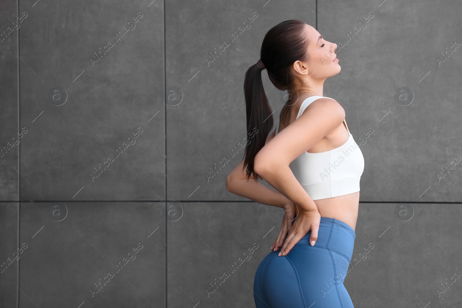 Photo of Beautiful woman in sportswear near dark grey wall. Space for text