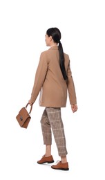 Young businesswoman with stylish bag walking on white background