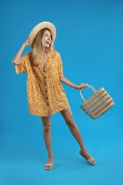 Photo of Young woman wearing stylish dress with straw bag on blue background